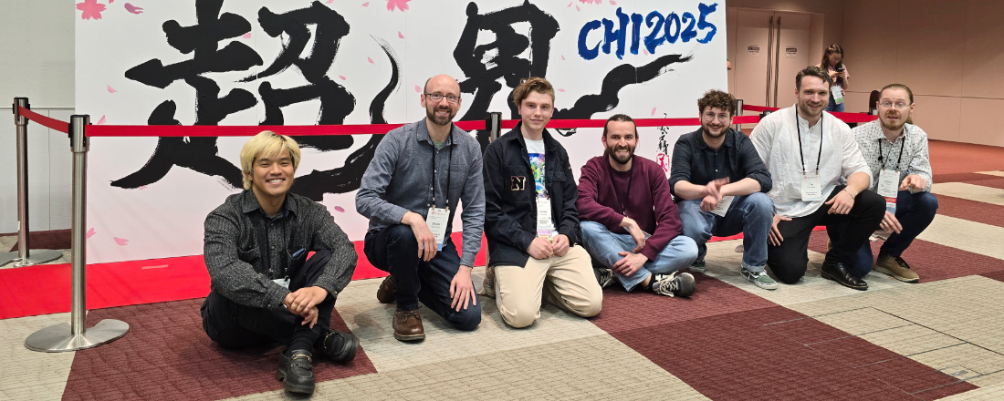 Group picture: UBT team in front of the CHI 2025 sign in the conference hall.
